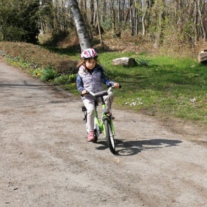 Mädchen fährt mit Fahrradhelm auf einem grünen Fahrrad einen Weg entlang. 