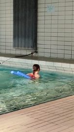 Ein Kind mit Schwimmnudel im Schwimmbecken.