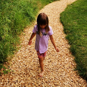 Ein Mädchen geht barfuß über einen Weg mit Holzspähnen